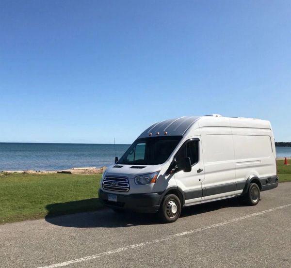 A white high-roof Westar passenger van parked by a lake on a sunny day.