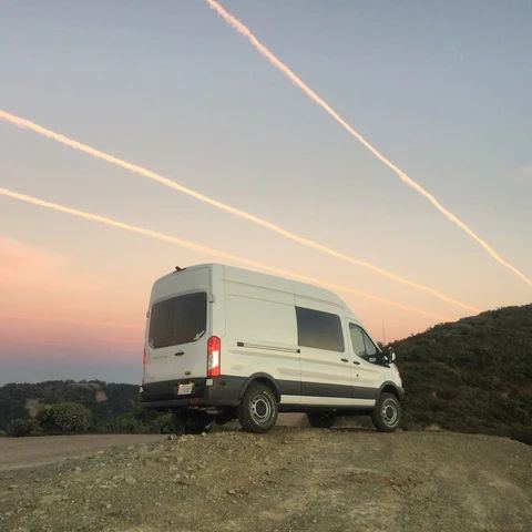 A white high-roof passenger van parked on a hilltop at sunset.